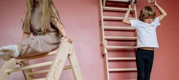 Two children engaged in play on wooden gym equipment indoors.