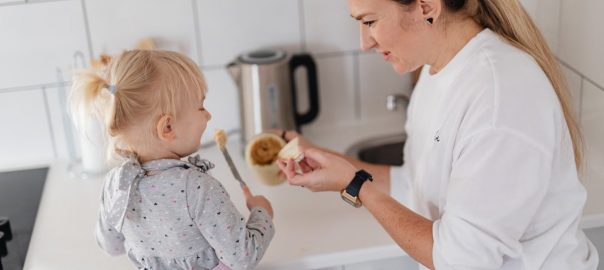 A mother and her young daughter interact while preparing food in a modern kitchen.