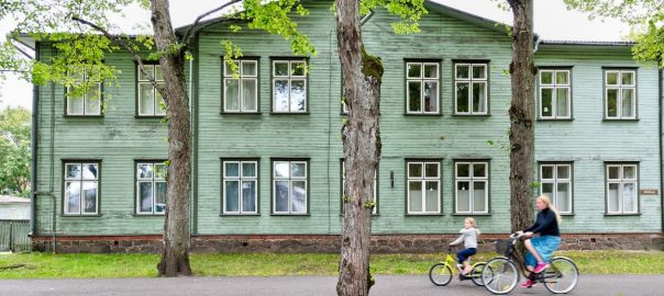 two cycling people passing gray wooden house